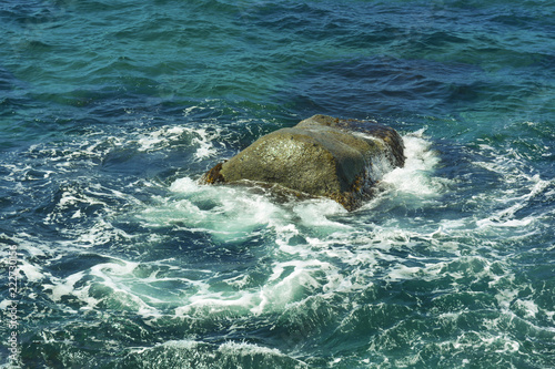 Stone in the sea, around white foam. Sea water and stone