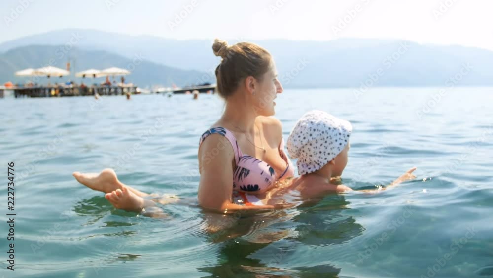 4k footage of beautiful young woman taching swimming her little boy in the sea