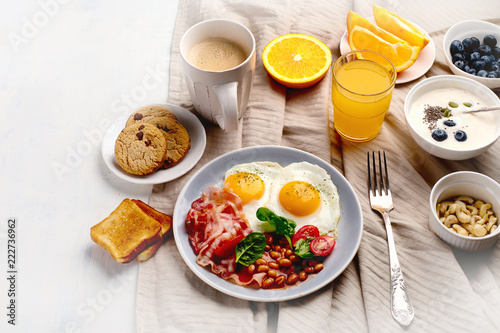 Breakfast with fried eggs, bacon, orange juice, yogurt and toasts