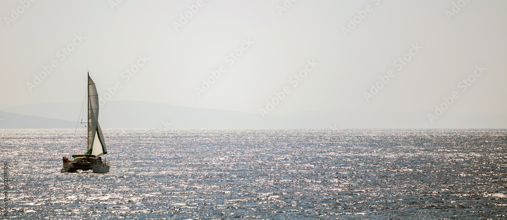 Sailboat travels with wind help in calm sea with bokeh sun light. Blue sky background, banner.
