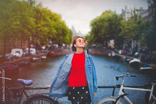 Canvas Print Young girl in red sweater and orange sunglasses with backpack at bridge in Amsterdam street