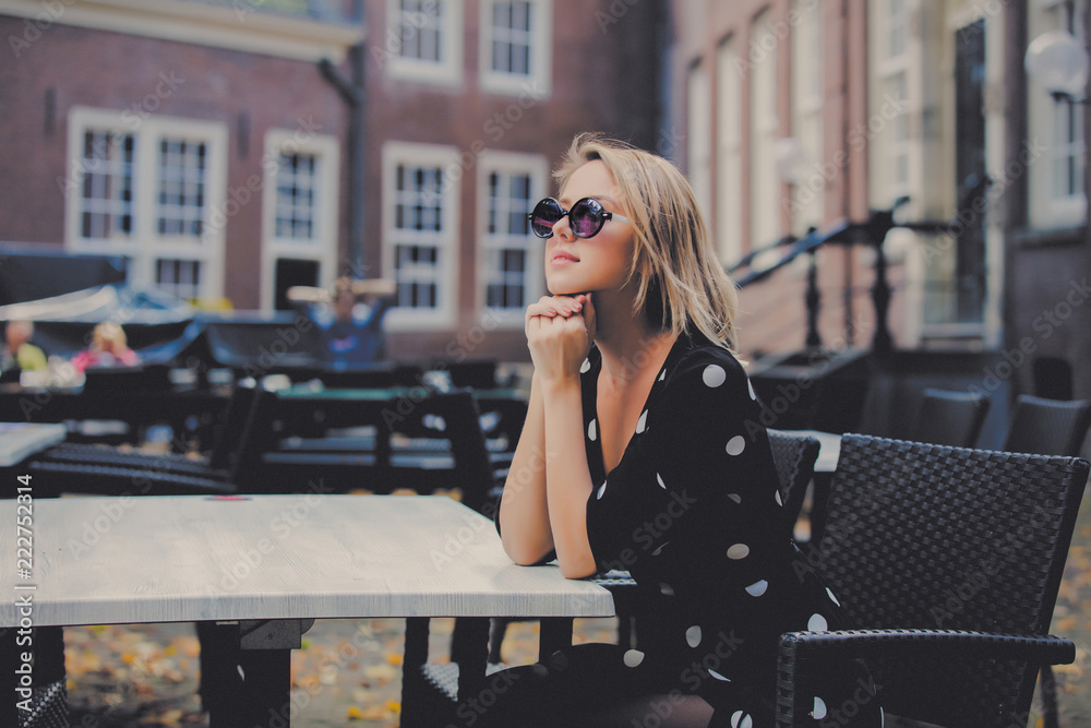Fototapeta premium Young girl in black dress and sunglasses in Amsterdam cafe. Holland, Netherlands