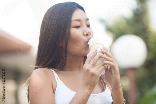 Happy young smiling asian brunette woman eating ice cream on green trees background in Park
