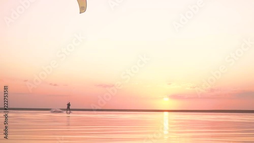 Silhouette of a male kiter who performs tricks on the water during sunset, slow motion photo