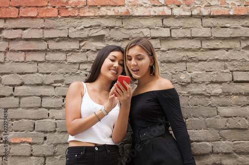 Two happy women friends sharing social media in a smart phone outdoors in a park