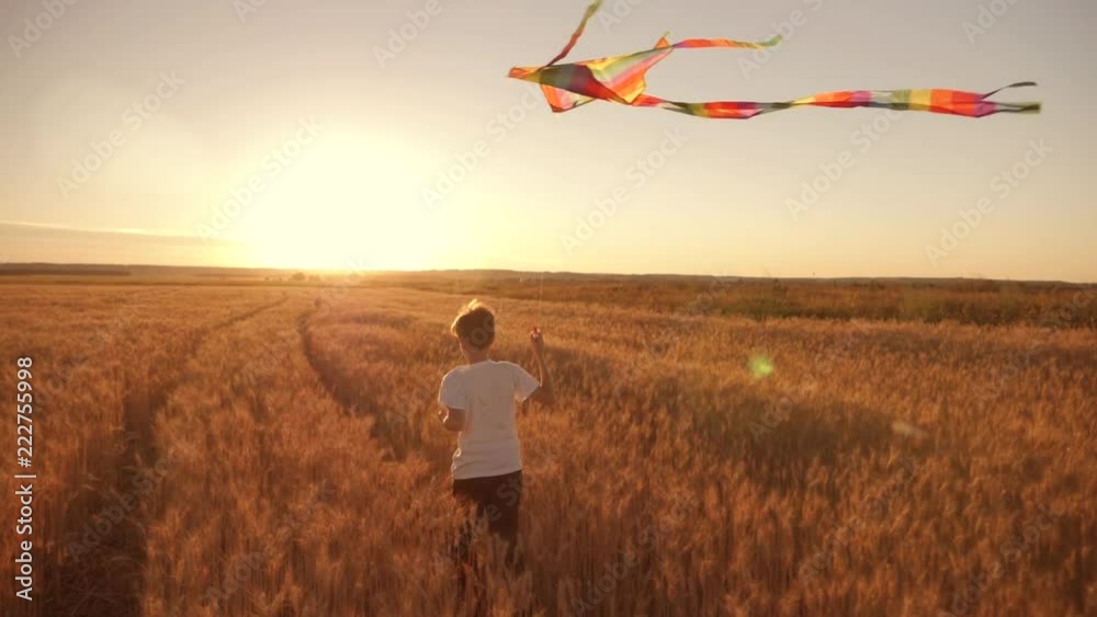A boy runs across the field at sunset with a kite flying over his head. A chidhood dream. Kids Games
