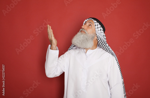 Fototapeta Naklejka Na Ścianę i Meble -  Senior Arab with a checkered veil pointing up and looking away isolated on red background