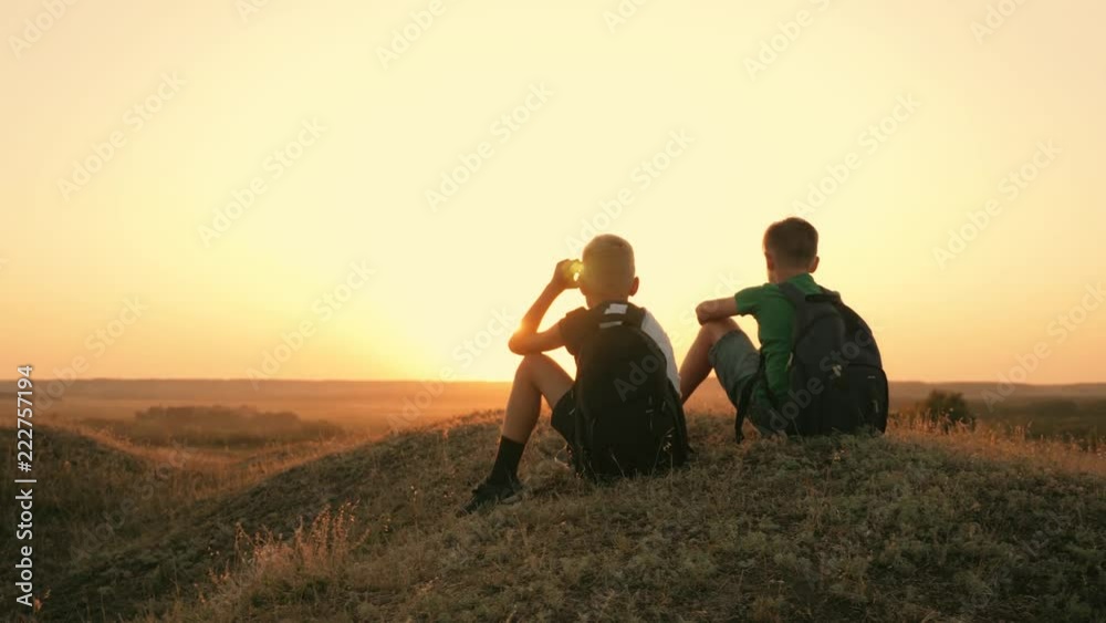 Two travelers boy. Two boys are walking along the field at sunset with rucksacks. The concept of family and travel Two travelers boy. Two boys are walking along the field at sunset with rucksacks. The concept of family and travel