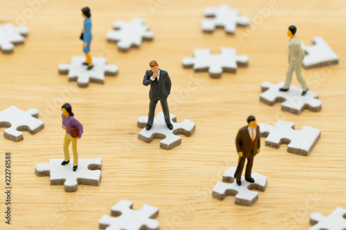 Miniature people businessmen standing on white Jigsaw. The concept used in selecting personnel to participate in the organization. with copy space.