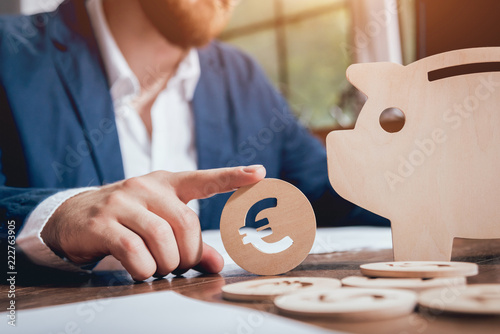 Businessman holds a coin near wooden piggy. Money box. Collecting money with earning bank. photo