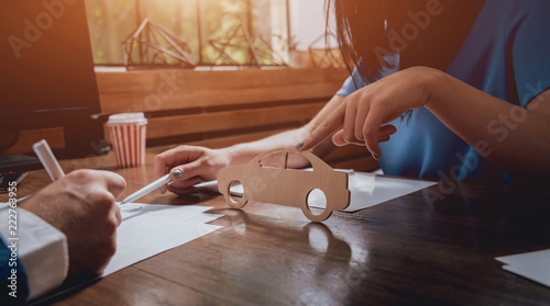 Foto Man signing a car insurance policy, the agent is holding the wooden car model