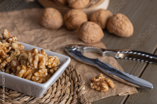 Walnuts in a white bowl and a nutcracker on the wooden table