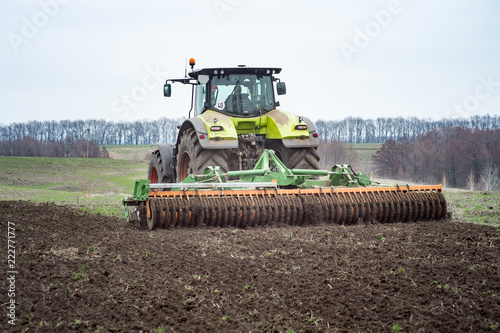 A tractor pulls a disc harrow system implement to smooth over a dirt field in preparation for planting