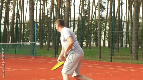 Rear view of active sporty man scoring apoint with overhead smash while playing tennis match on hardcourt. Male tennis player hitting smash to win a point on outdoor court. Slow motion. photo