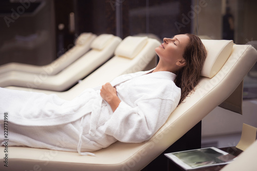 Rest and comfort. Side view portrait of attractive woman with closed eyes relaxing at spa salon. She is wearing white soft bathrobe