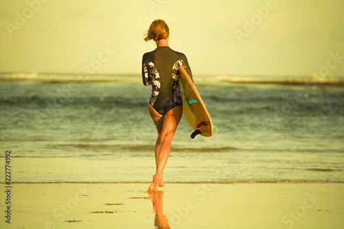 Photography back view of young attractive and sporty surfer girl in cool swimsuit at the bea