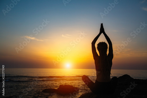Yoga silhouette woman meditation on the ocean during amazing sunset.
