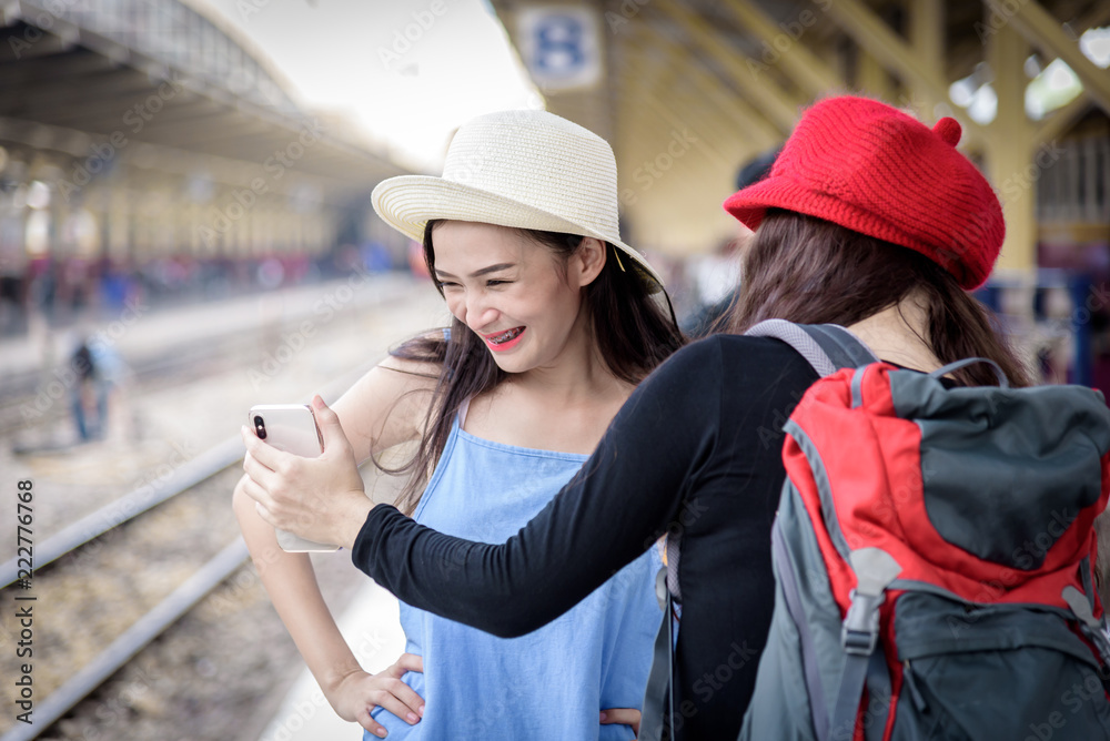 Asian women traveler have playing a mobile phone and talking for waiting the train with happiness at Hua Lamphong station at Bangkok, Thailand.