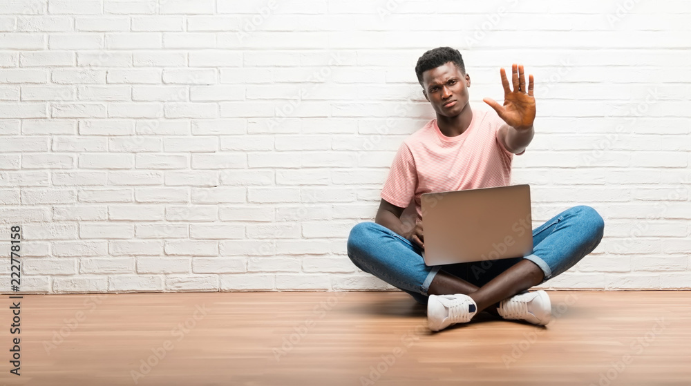 Afro american man sitting on the floor with his laptop making stop gesture with her hand