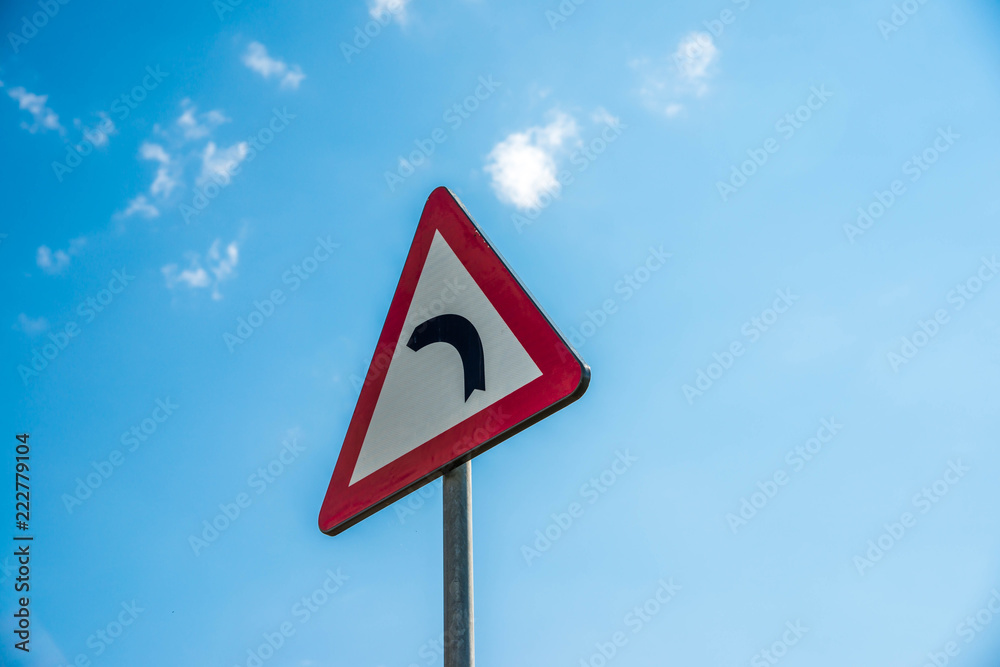 Left curve traffic sign close up, beautiful blue sky background. Left curve traffic sign close up, beautiful blue sky background.