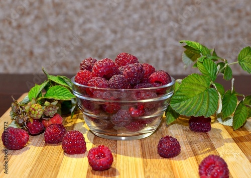 Juicy fresh raspberry berries lie in a glass bowl and on a table with green leaves, a natural delicious fragrant meal