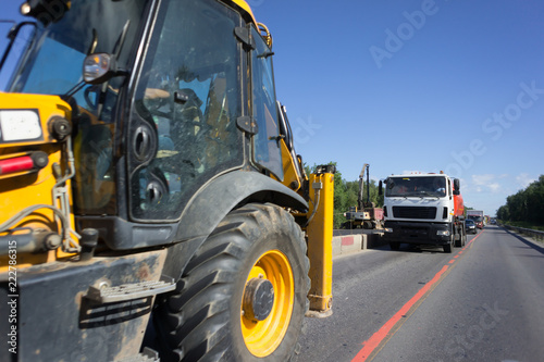 Tractor rides on the asphalt road with red and white safety concrete blocks