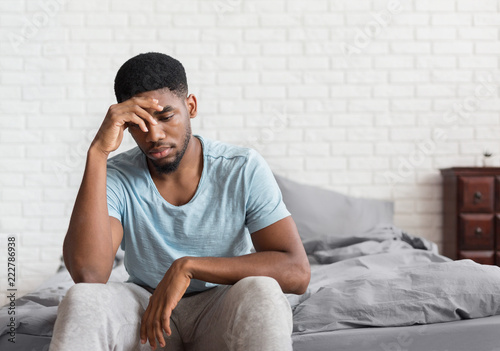 Young depressed black man sitting on bed