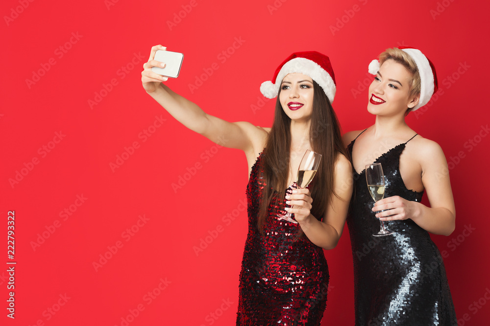 Plakat Happy girls in santa hats taking selfie on smartphone