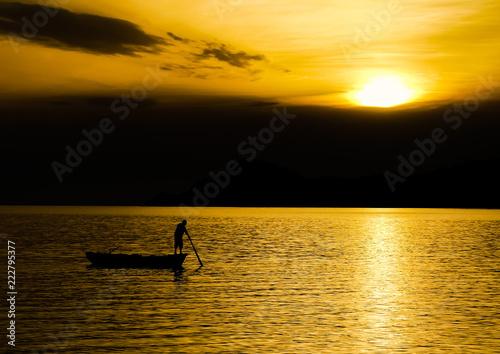 Silhouette of unidentifiable boatman checking fishing nets in Lopud bay with sun setting over Sipan island, Croatia