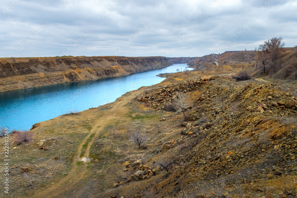 The old abandoned sandstone quarry with long blue lake and unpaved road at the bottom