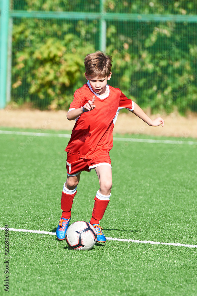 Boy soccer player with ball on football field