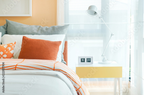 White foldable reading lamp on night table next to bed in orange and gray bedding style