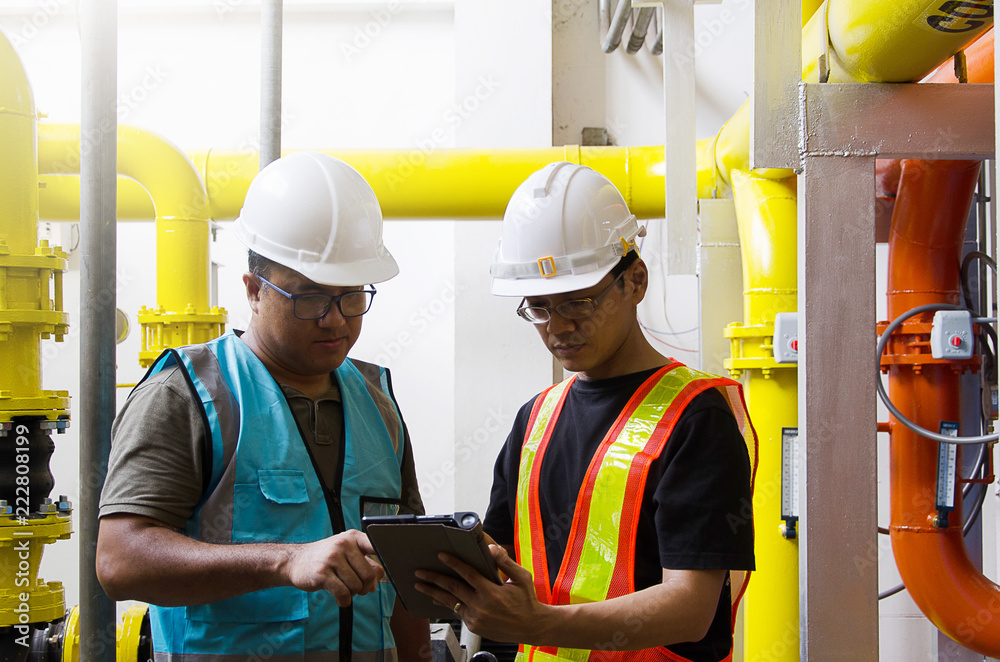 Two Male Industrial Engineers in Hard Hats Discuss New Project while Using Laptop Two Male Industrial Engineers in Hard Hats Discuss New Project while Using Laptop