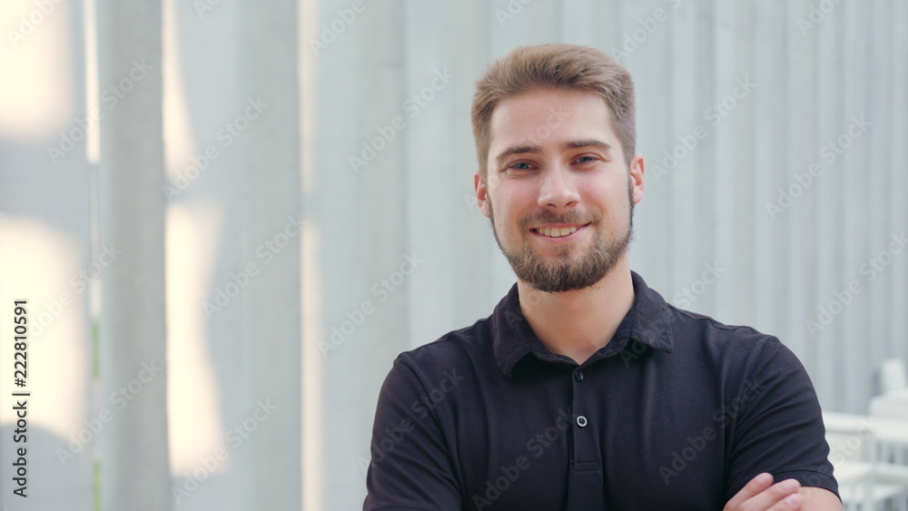 A happy smiling man with a beard standing arms crossed against a white blurry background. Medium shot. Soft focus A happy smiling man with a beard standing arms crossed against a white blurry background. Medium shot. Soft focus