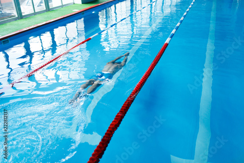 Photo on top of sports man in blue cap swimming on path in pool under water