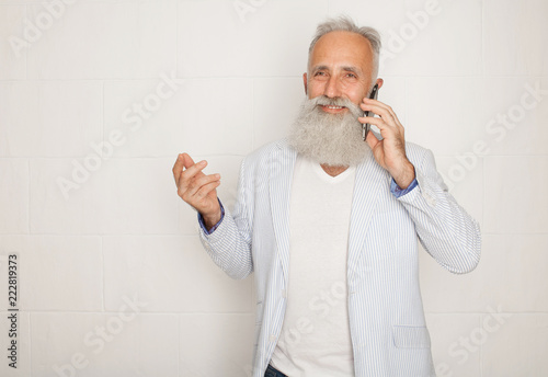 Studio shot of happy senior bearded businessman smiling while using mobile phone with against white background