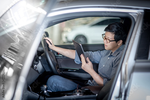 Young Asian businessman with glasses reading news on digital tablet while sitting on driver seat in his car. Business and technology concept © zephyr_p