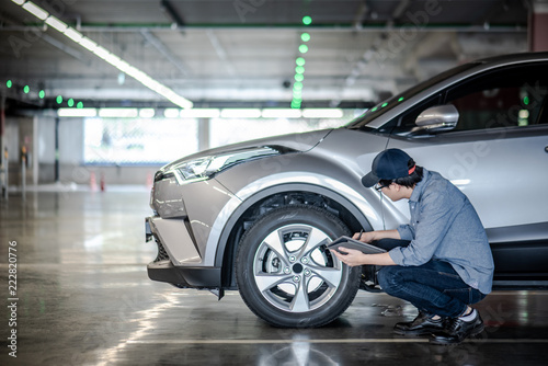 Obraz na plátně Young Asian auto mechanic holding digital tablet checking car wheel in auto service garage