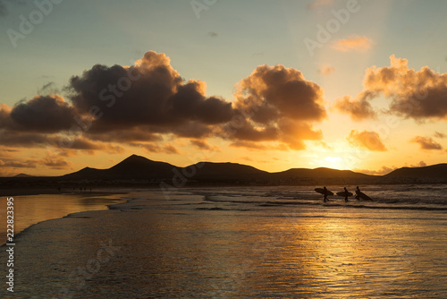 Three surfers at sunset come out of the ocean with a sense of pleasure and joy