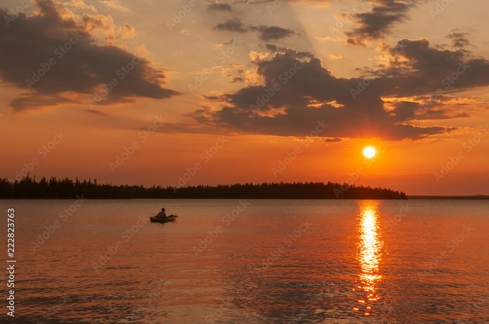 a large round sun is reflected in the smooth water of the lake and the silhouette of a fisherman in a boat