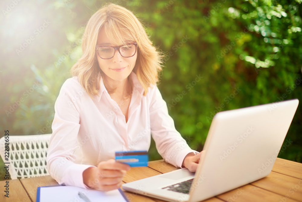 Woman using credit card and laptop at home outside on terrace. Outdoor portrait.