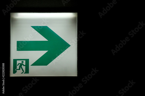 an emergency exit way sign board on the dark room wall background.