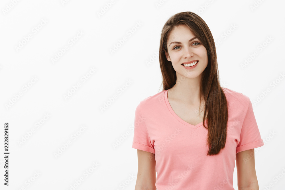 Waist-up shot of happy carefree beautiful caucasian woman in pink t-shirt, smiling broadly and gazing at camera with friendly and trustful expression, standing over gray background Waist-up shot of happy carefree beautiful caucasian woman in pink t-shirt, smiling broadly and gazing at camera with friendly and trustful expression, standing over gray background