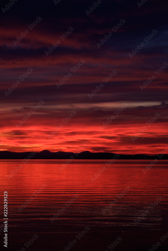 red and hot sunset at Balaton lake - clouds, thin waves on water and hills in background - dark tones, vertical