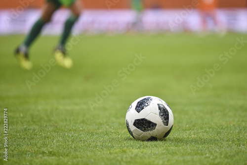 Ball on the football pitch and players legs i the background.