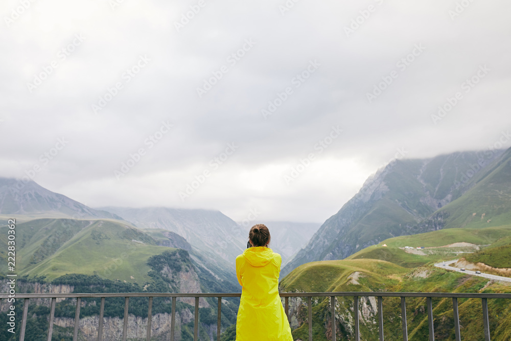 A young Girl in a yellow raincoat photographs the mountains. Georgia. Summer. August. Girl making a photo shoot of mountain. 