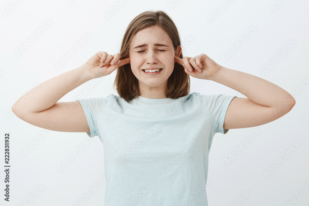 Make this sound stop. Unhappy insecure crying cute girl with brown hair closing eyes and clenching teeth making displeased sad expression covering ears with index fingers not hear parents fighting Make this sound stop. Unhappy insecure crying cute girl with brown hair closing eyes and clenching teeth making displeased sad expression covering ears with index fingers not hear parents fighting