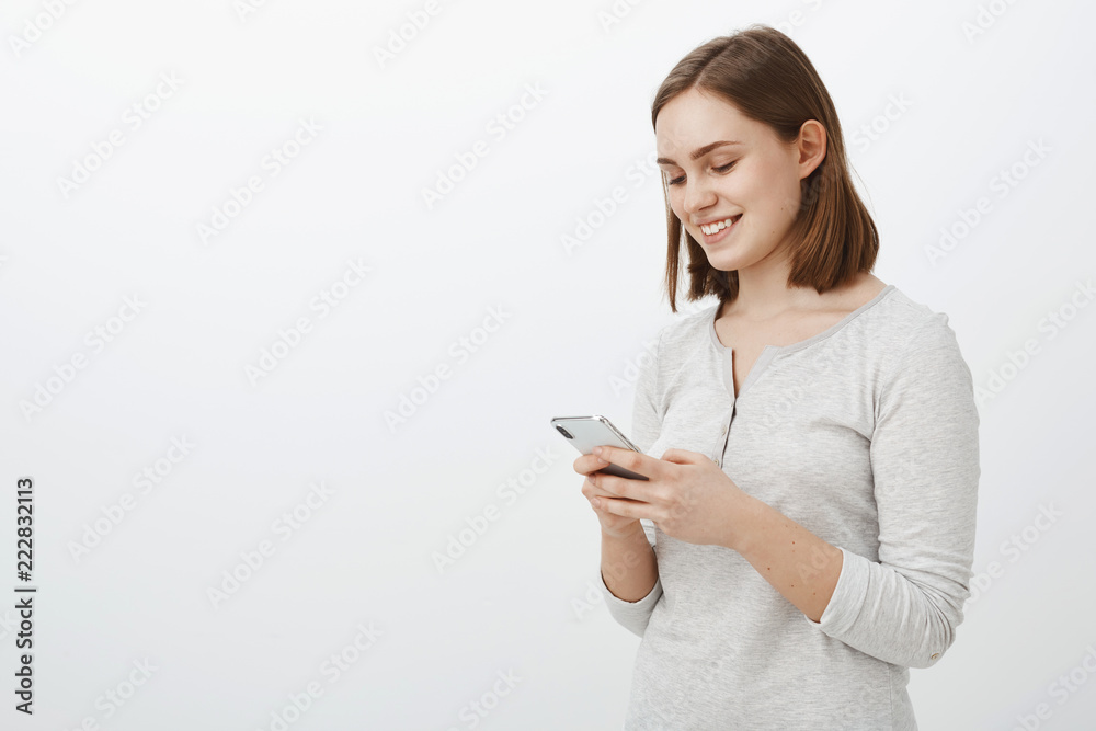 Waist-up shot of sociable carefree female internet geek smiling joyfully while having amusing chat in network with best friend from online game holding smartphone and smiling at cellphone screen Waist-up shot of sociable carefree female internet geek smiling joyfully while having amusing chat in network with best friend from online game holding smartphone and smiling at cellphone screen