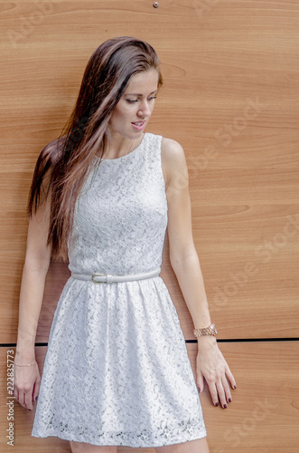 Young girl in a white dress near a wooden wall
