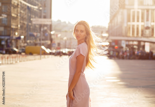 Wonderful blonde model with flying hair posing at the street in sun beam. Female fashion concept. Space for text